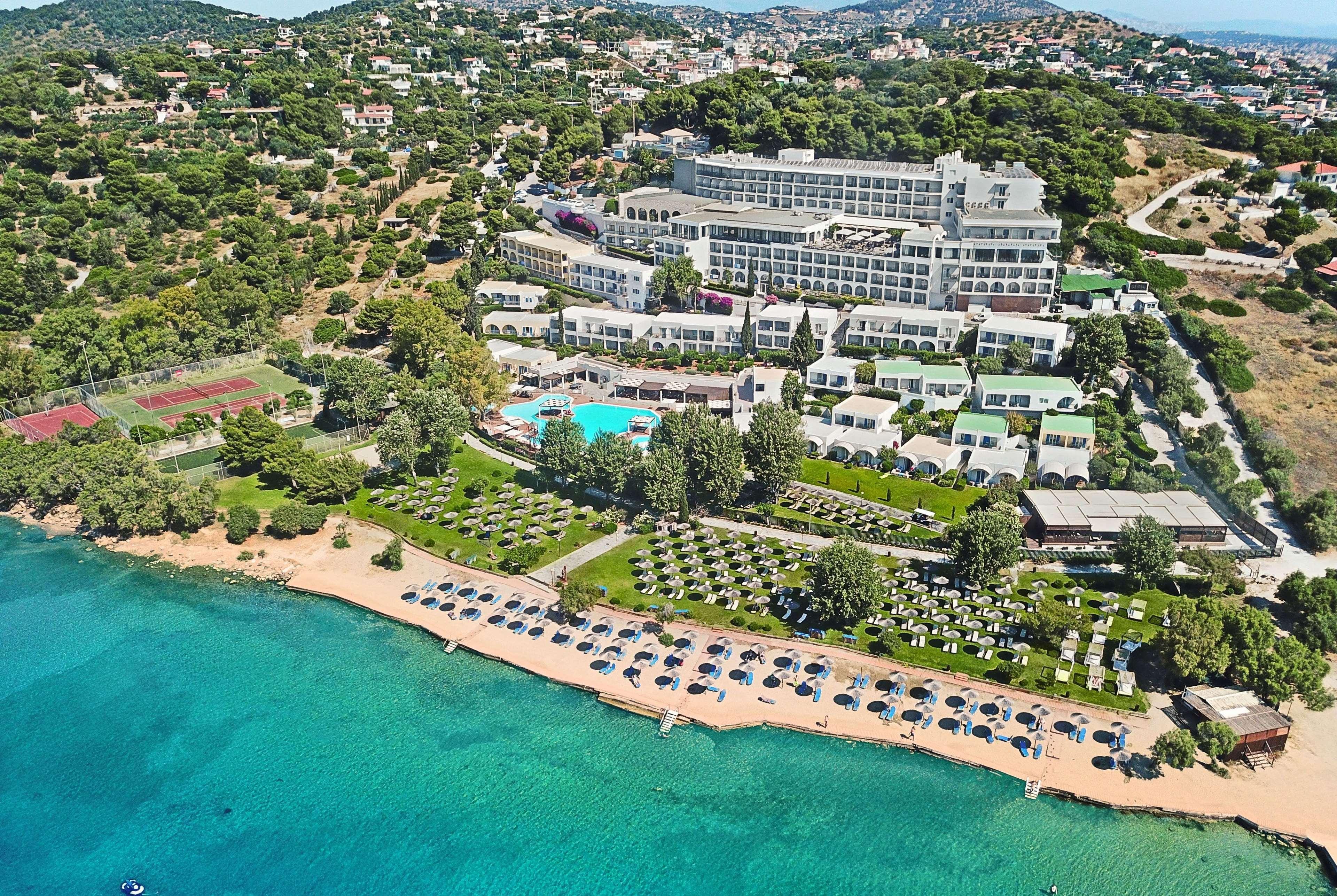 Hotel Dolce By Wyndham Athens Attica Riviera Vravrona Exterior foto The photo shows a scenic aerial view of a resort located near a beautiful coastline. The resort features a large building and various smaller accommodations. An inviting swimming pool is visible at the center, surrounded by sun loungers and greenery.
