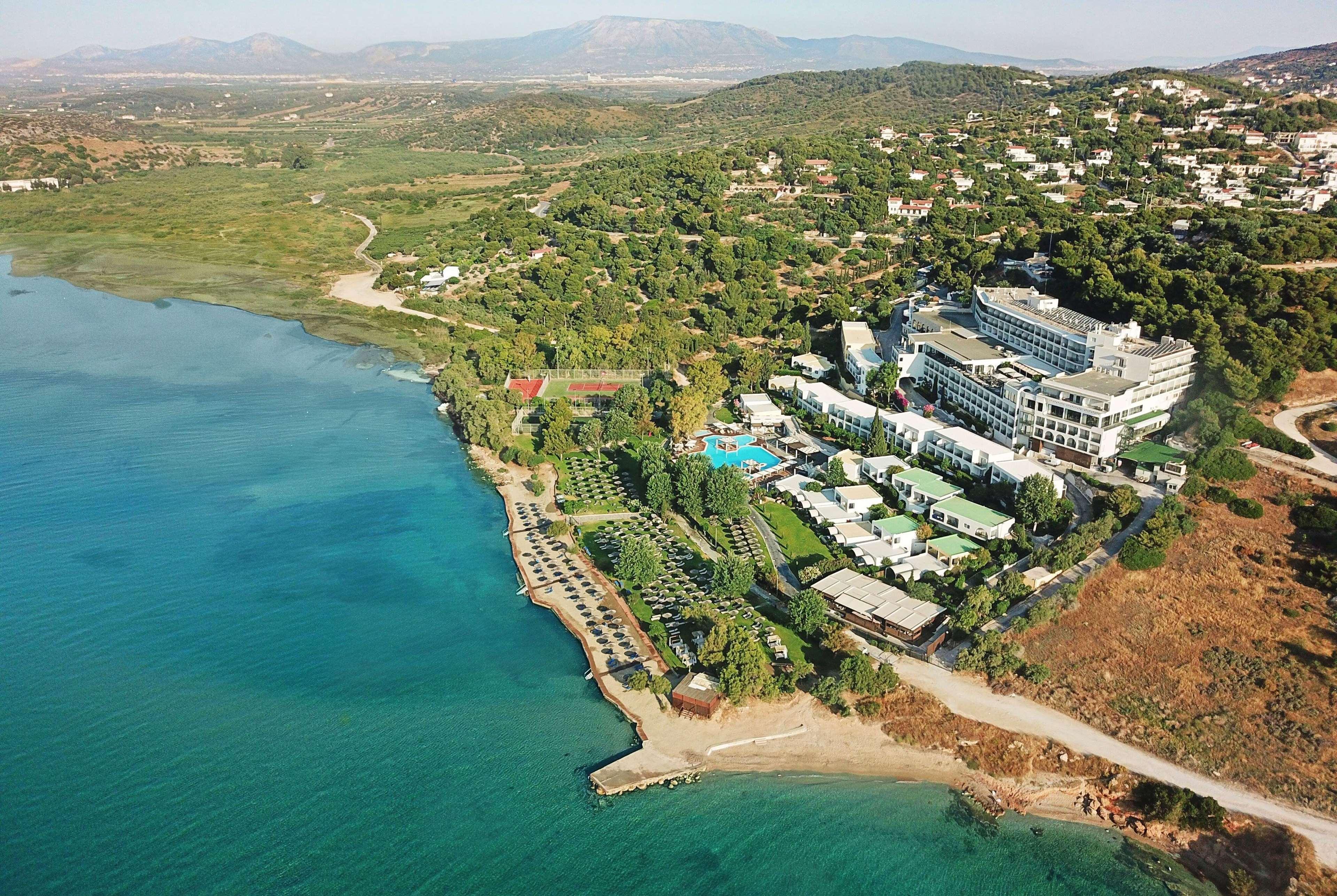 Hotel Dolce By Wyndham Athens Attica Riviera Vravrona Exterior foto The photo shows an aerial view of a coastal area featuring a resort or hotel complex situated near the shoreline. The building has multiple levels and is surrounded by lush greenery and landscaped gardens. There is a pool area visible, as well as sev