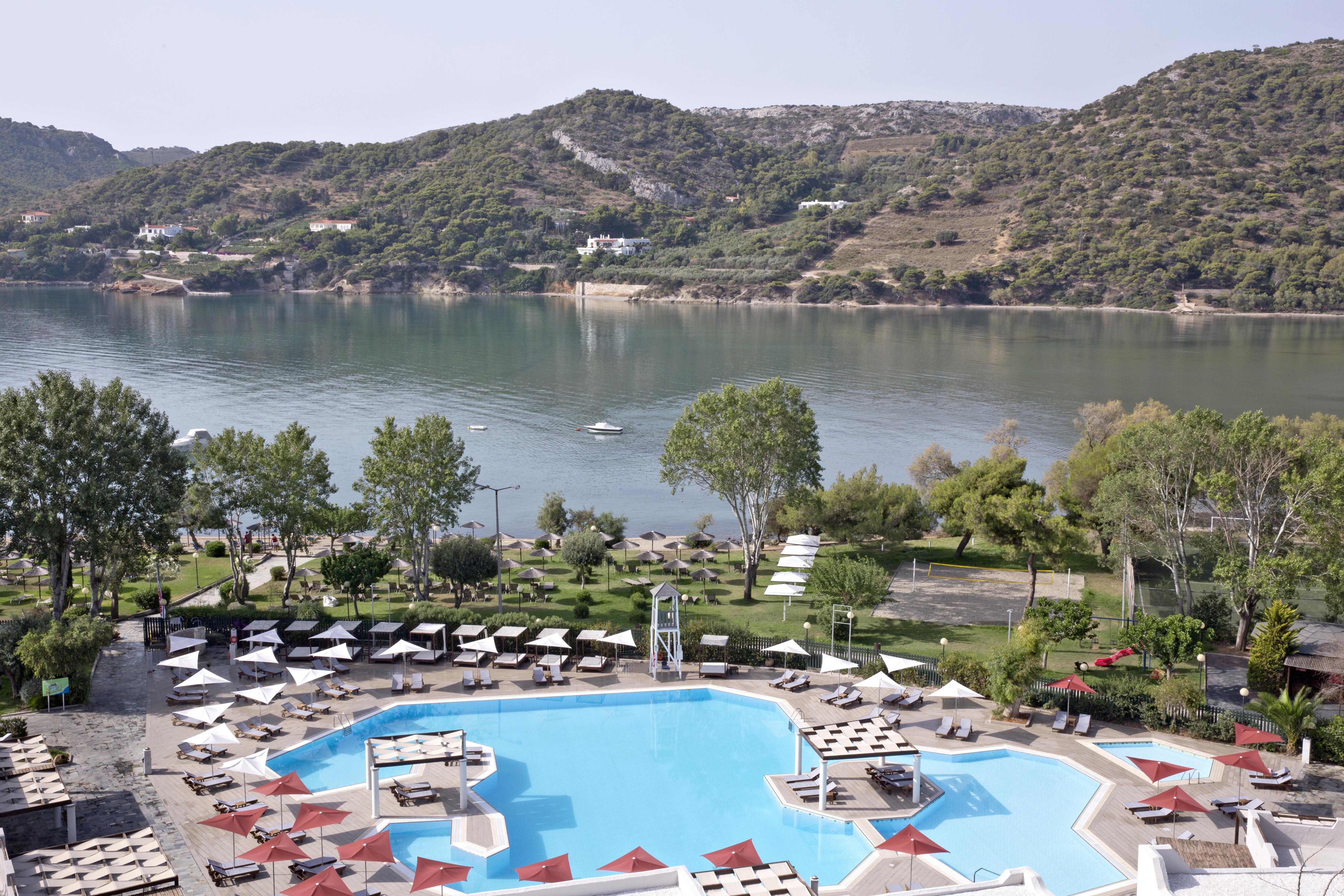 Hotel Dolce By Wyndham Athens Attica Riviera Vravrona Exterior foto The photo depicts a serene view of a resort area featuring a large swimming pool in the foreground. The pool has a unique octagonal shape and is surrounded by sun loungers and umbrellas, creating a relaxing atmosphere. Beyond the pool, there is a cal
