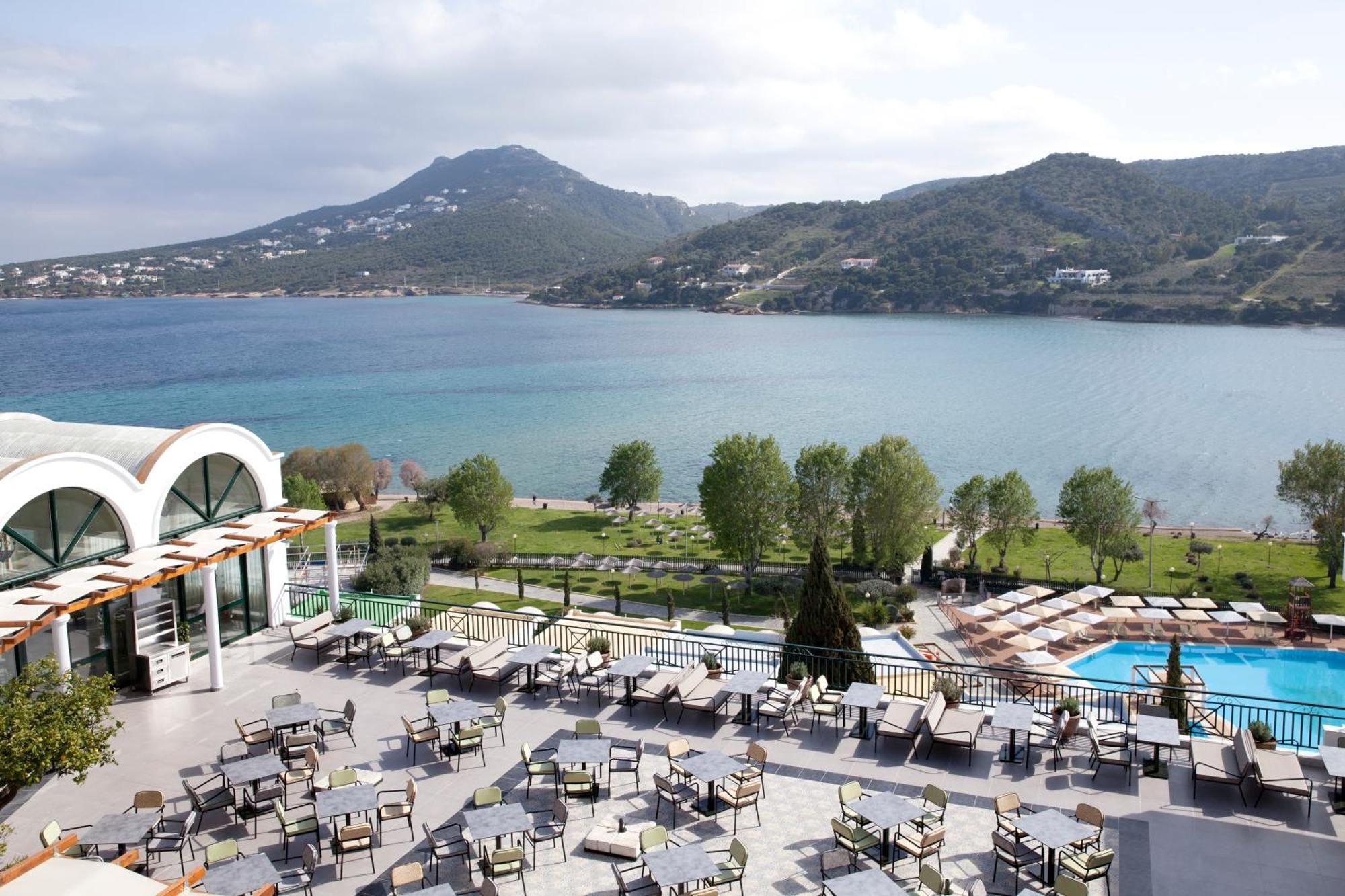 Hotel Dolce By Wyndham Athens Attica Riviera Vravrona Exterior foto The photo depicts a scenic view from a terrace or outdoor dining area. In the foreground, there are numerous tables and chairs arranged neatly, likely for guests to enjoy meals or drinks. Beyond the seating area, a swimming pool can be seen. 

In the