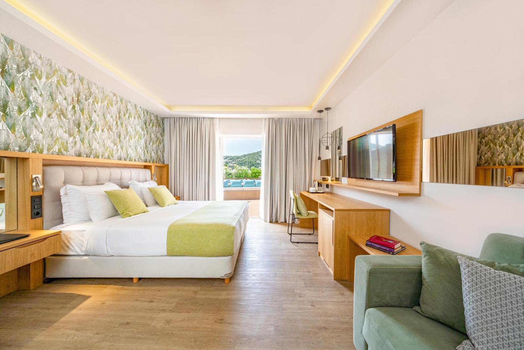 Hotel Dolce By Wyndham Athens Attica Riviera Vravrona Exterior foto The photo shows a modern hotel room featuring a large bed with white linens and accent pillows in light green. Behind the bed is a decorative wall with floral patterns. On one side of the room, there is a comfortable chair and a small side table. Acr